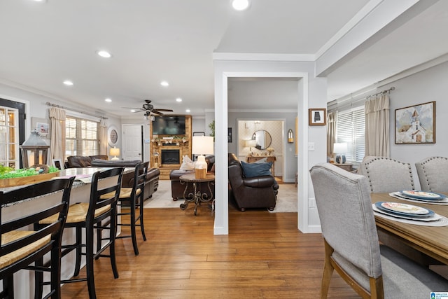 dining area with crown molding, recessed lighting, light wood-style flooring, a fireplace, and a ceiling fan