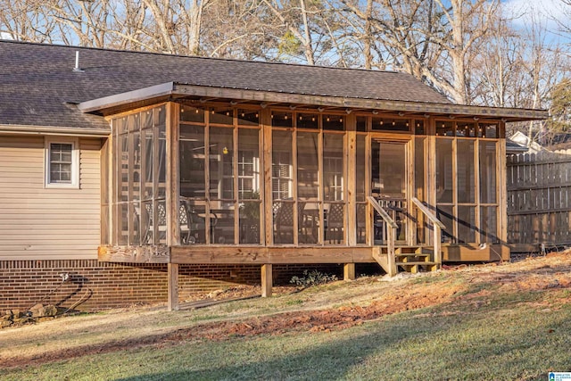 rear view of house featuring fence, roof with shingles, and a sunroom