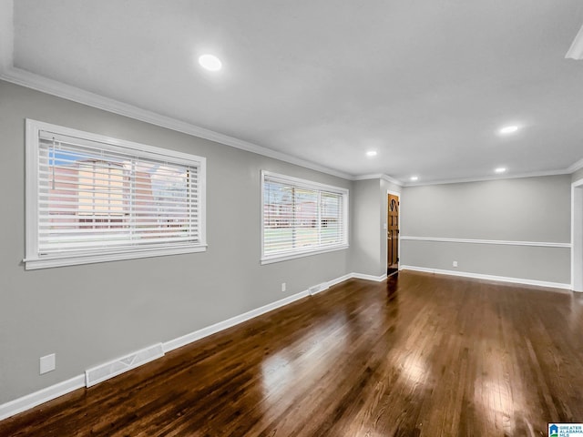 empty room featuring wood finished floors, baseboards, visible vents, and ornamental molding