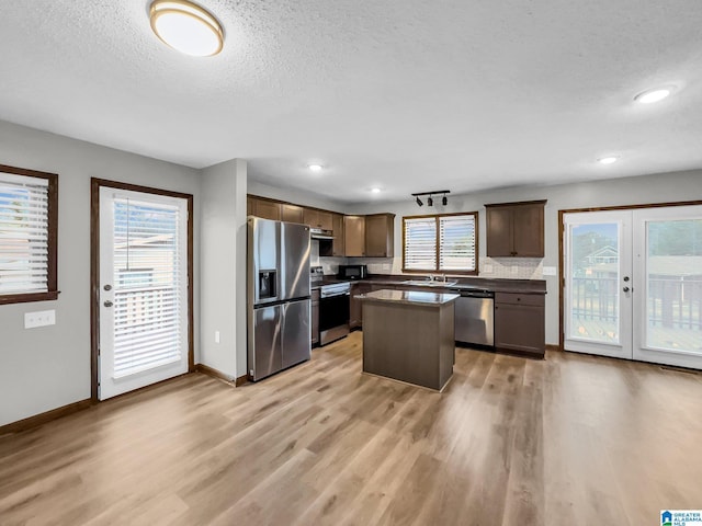 kitchen with baseboards, a kitchen island, light wood-style flooring, stainless steel appliances, and dark countertops