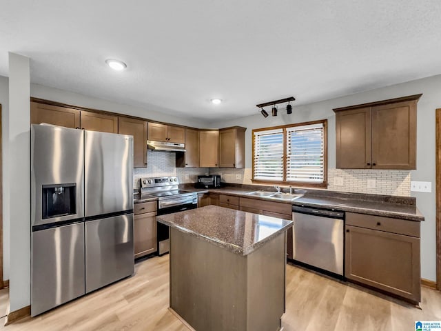 kitchen with under cabinet range hood, appliances with stainless steel finishes, tasteful backsplash, and light wood-style floors