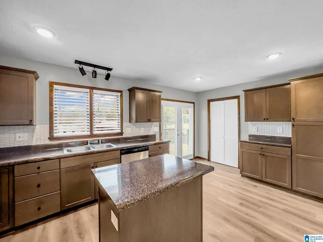 kitchen with stainless steel dishwasher, decorative backsplash, light wood-style flooring, and a sink