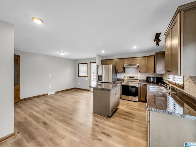 kitchen featuring a kitchen island, a sink, decorative backsplash, stainless steel appliances, and under cabinet range hood