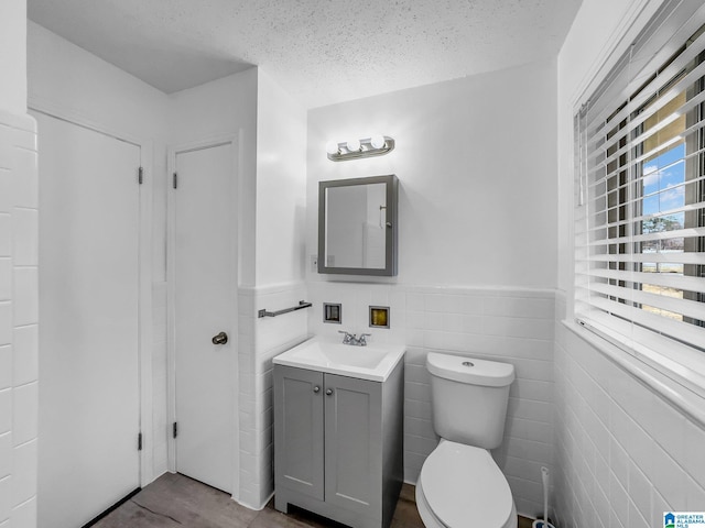 half bathroom featuring a wainscoted wall, toilet, a textured ceiling, and vanity