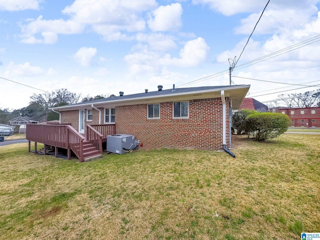 rear view of property featuring a yard, brick siding, central AC, and a wooden deck