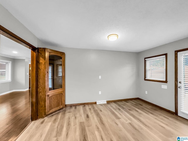 unfurnished room with light wood finished floors, visible vents, a wealth of natural light, and baseboards