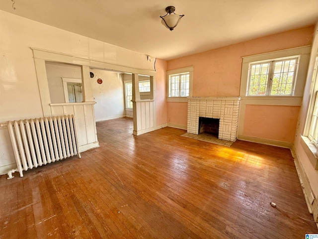 unfurnished living room featuring hardwood / wood-style floors, radiator, a fireplace, and baseboards