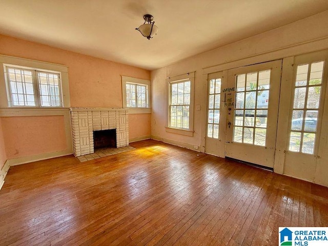 unfurnished living room with hardwood / wood-style flooring, a brick fireplace, and baseboards