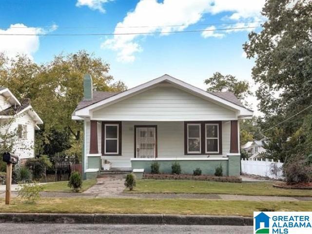 bungalow featuring a front yard, a porch, fence, and a chimney