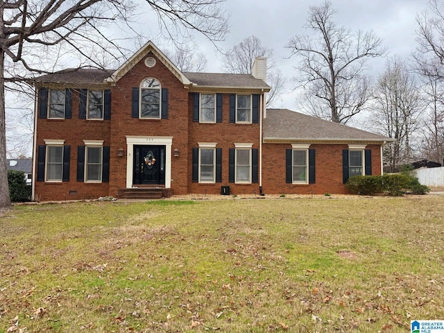 colonial home with crawl space, a front lawn, brick siding, and a chimney