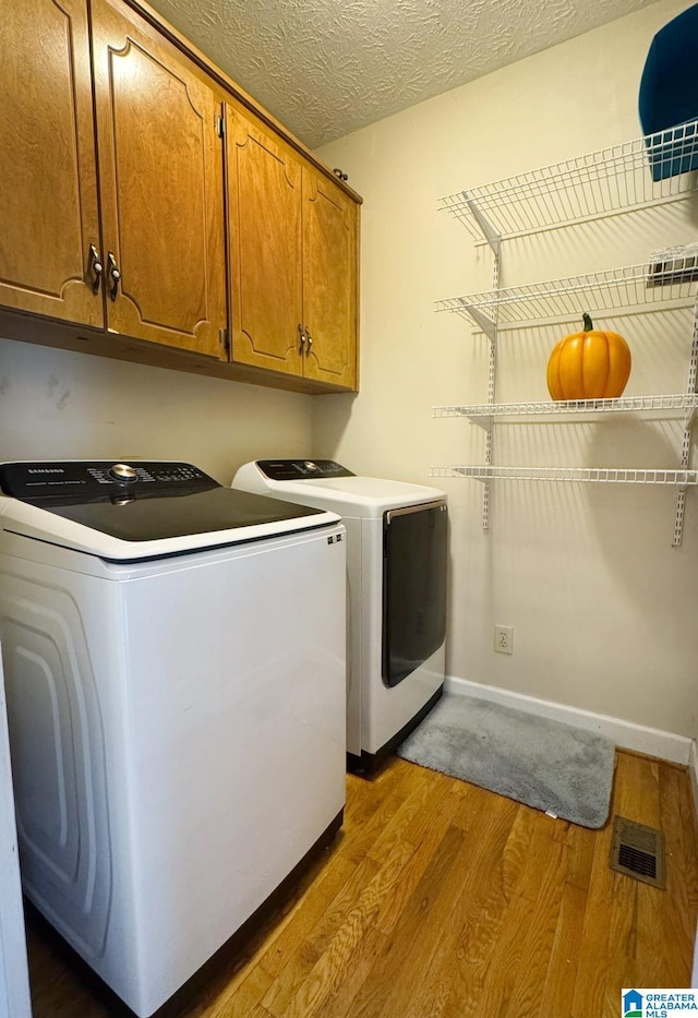 laundry room featuring visible vents, light wood-style flooring, cabinet space, a textured ceiling, and independent washer and dryer