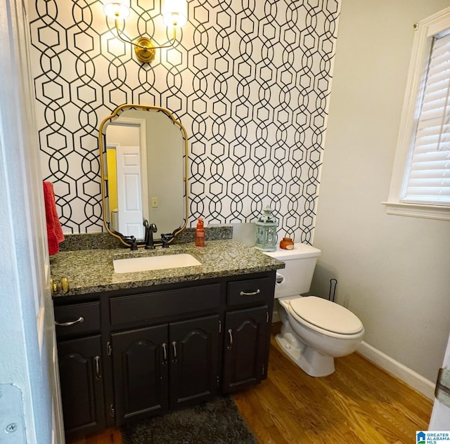 half bath featuring vanity, toilet, wood finished floors, and baseboards