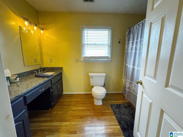 full bath featuring baseboards, toilet, vanity, wood finished floors, and a textured ceiling