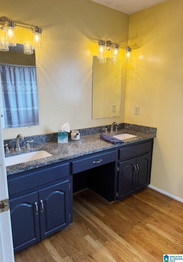 full bath featuring a sink, baseboards, wood finished floors, and double vanity