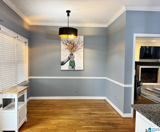 unfurnished dining area featuring a brick fireplace, wood finished floors, baseboards, and ornamental molding