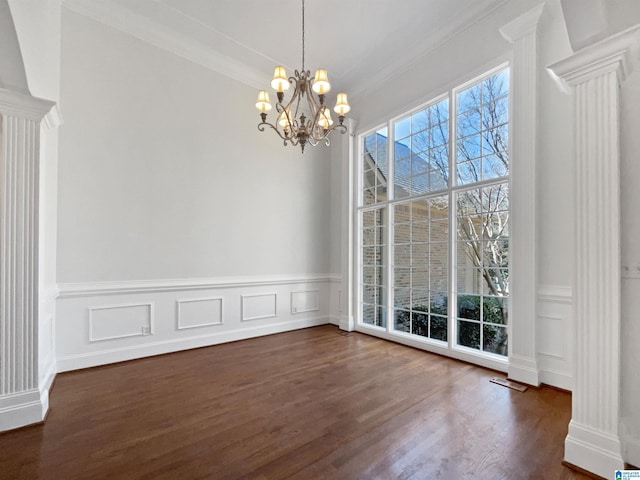 unfurnished dining area featuring dark wood-style floors, a chandelier, a decorative wall, and ornate columns