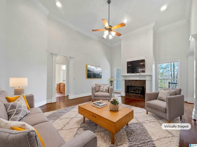 living area featuring arched walkways, a fireplace with flush hearth, ornamental molding, and wood finished floors