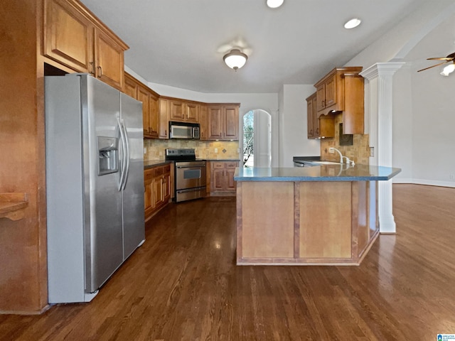 kitchen featuring brown cabinetry, a peninsula, arched walkways, stainless steel appliances, and a sink