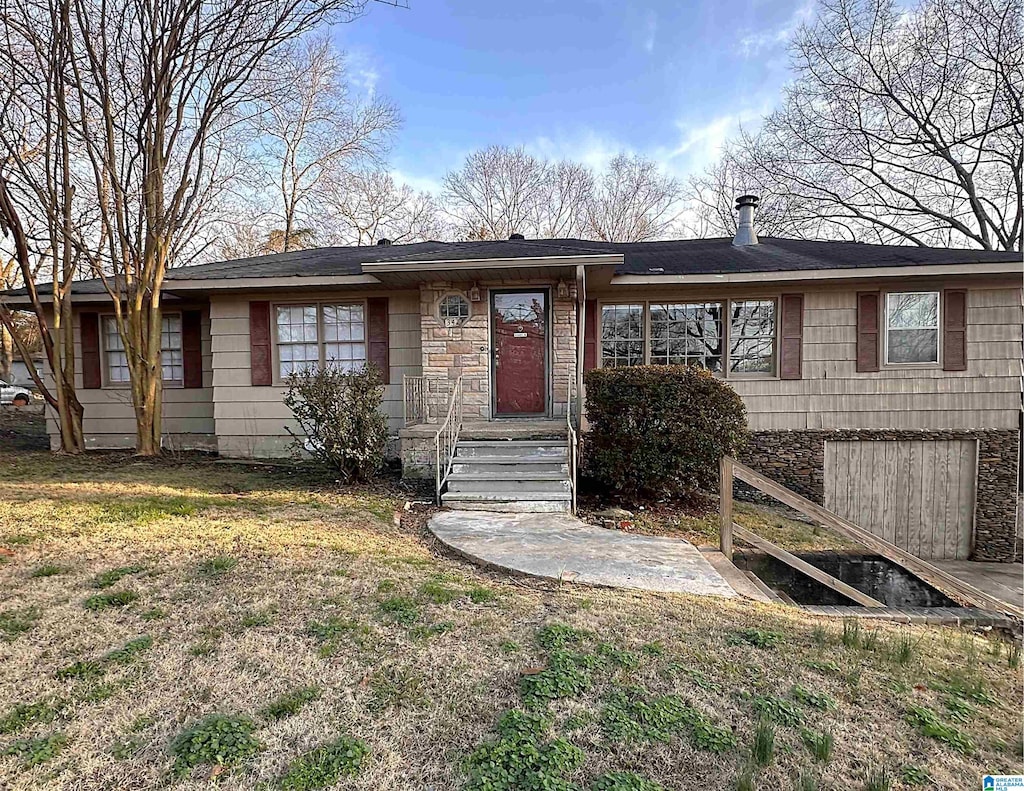 single story home featuring a garage, stone siding, and a front yard