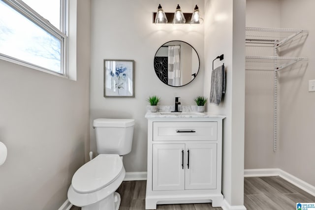 bathroom with toilet, vanity, baseboards, and wood finished floors