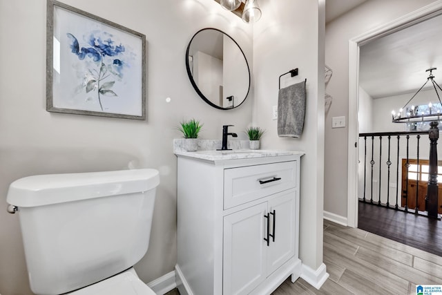 bathroom with baseboards, toilet, wood finished floors, a notable chandelier, and vanity