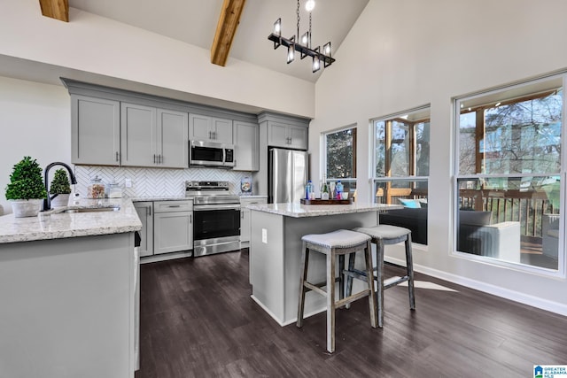 kitchen featuring light stone counters, a breakfast bar, gray cabinets, a sink, and stainless steel appliances