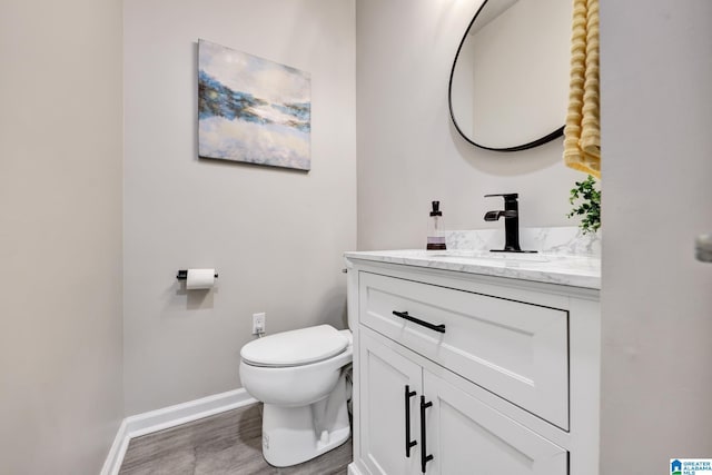 bathroom featuring baseboards, toilet, wood finished floors, and vanity