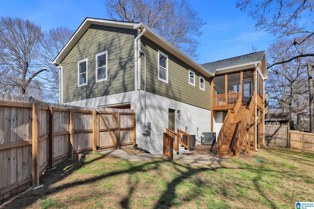 back of property with central air condition unit, a lawn, a fenced backyard, a sunroom, and stairs