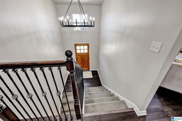 staircase with an inviting chandelier, wood finished floors, baseboards, and a towering ceiling