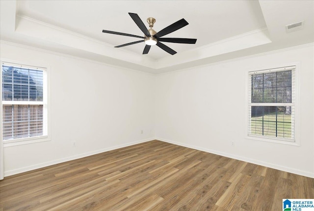 empty room with a tray ceiling, baseboards, visible vents, and wood finished floors