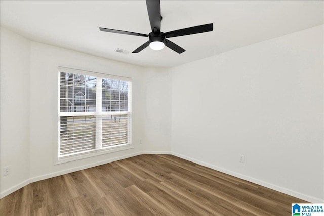 empty room featuring ceiling fan, visible vents, baseboards, and wood finished floors