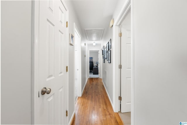 hall with attic access, light wood-style flooring, and baseboards