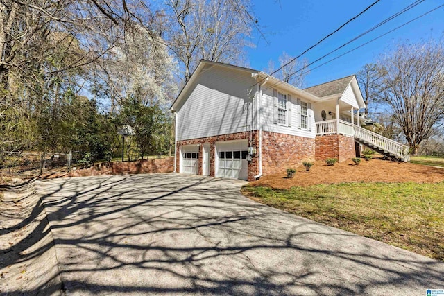 view of property exterior featuring driveway, covered porch, a garage, brick siding, and stairs