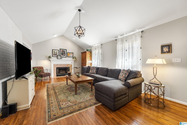 living room featuring baseboards, a fireplace with flush hearth, lofted ceiling, and wood finished floors