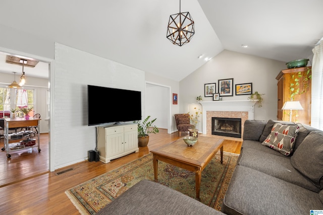 living room with visible vents, light wood-style floors, a fireplace, and vaulted ceiling