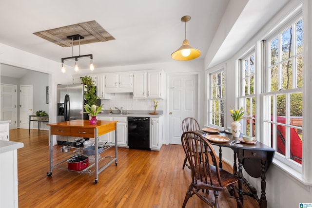 kitchen with light wood-style flooring, a sink, light countertops, black dishwasher, and backsplash