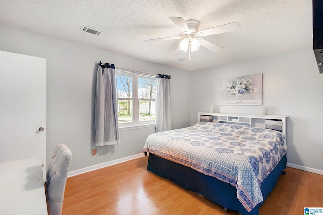 bedroom featuring light wood-type flooring, visible vents, a textured ceiling, baseboards, and ceiling fan