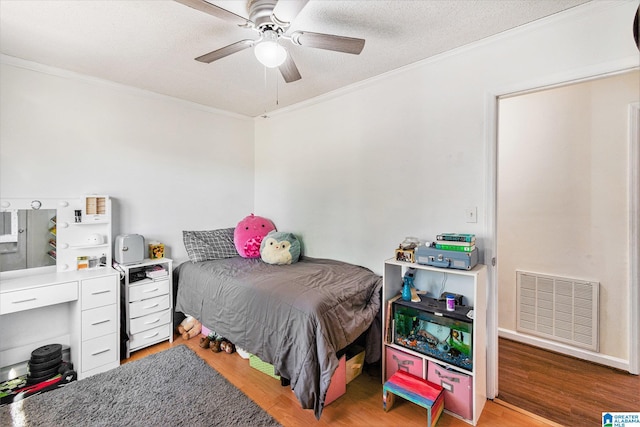 bedroom with visible vents, a textured ceiling, wood finished floors, and ornamental molding