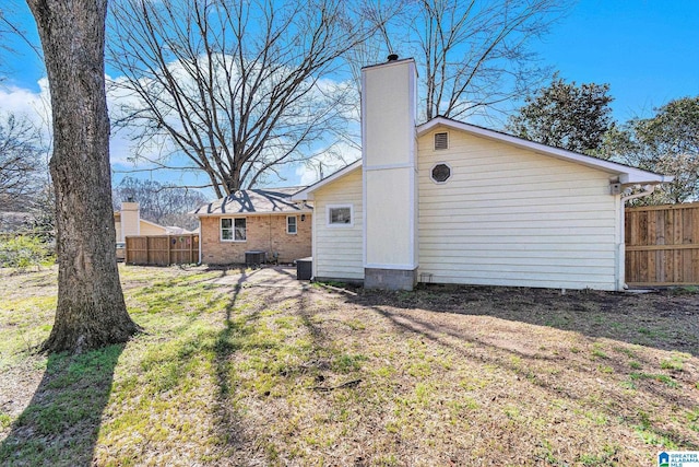 back of house with cooling unit, a lawn, a chimney, and fence