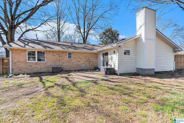 rear view of house with a patio, central AC, fence, brick siding, and a chimney