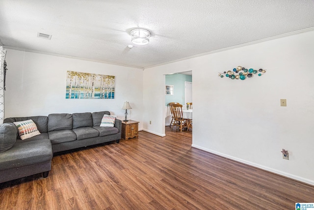 living room featuring visible vents, ornamental molding, a textured ceiling, wood finished floors, and baseboards