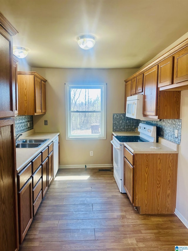 kitchen featuring tasteful backsplash, white appliances, wood finished floors, and a sink