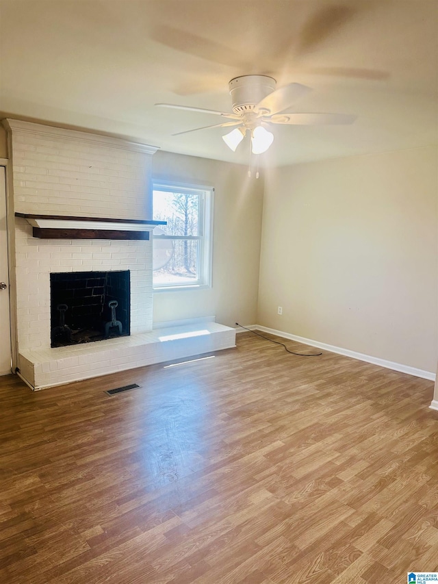 unfurnished living room featuring a brick fireplace, wood finished floors, and visible vents