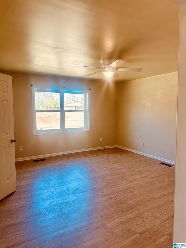 unfurnished room featuring baseboards, wood finished floors, visible vents, and ceiling fan
