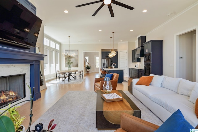 living room with crown molding, recessed lighting, ceiling fan with notable chandelier, and light wood-type flooring