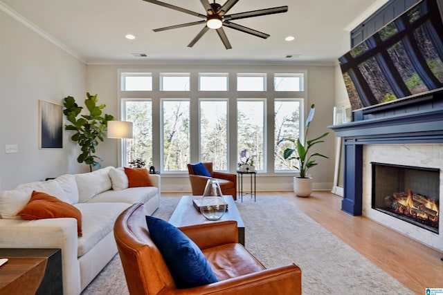 living area featuring a ceiling fan, baseboards, a fireplace, light wood-style floors, and crown molding