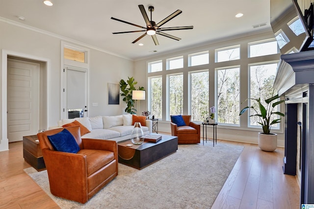 living room featuring crown molding, light wood-style flooring, a ceiling fan, and visible vents