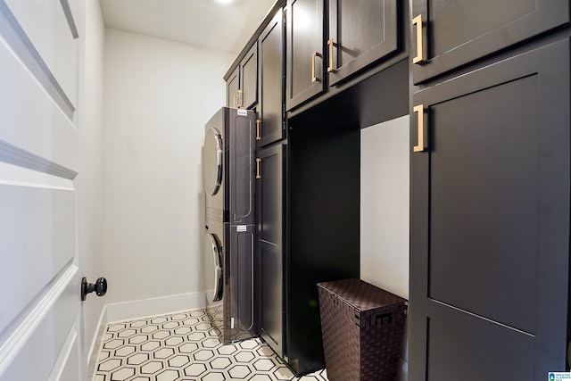 laundry room featuring cabinet space, stacked washer and clothes dryer, and baseboards