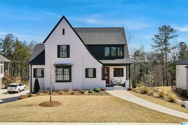 view of front of property featuring brick siding, a porch, a shingled roof, and a front yard