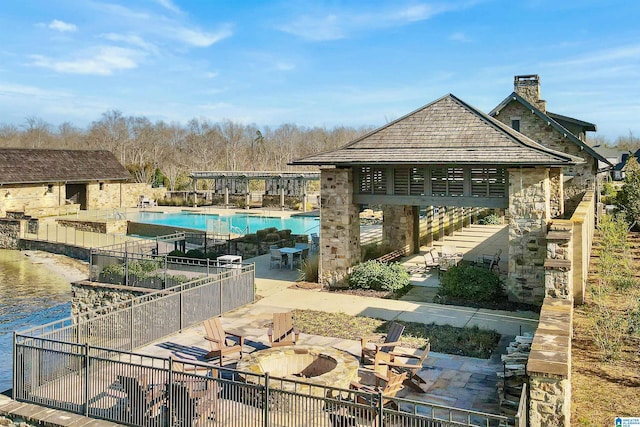 community pool featuring a patio area, fence, a water view, and an outdoor fire pit